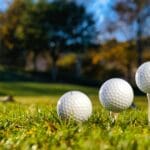Three golf balls on tees ready for play on a bright sunny day in a green field.