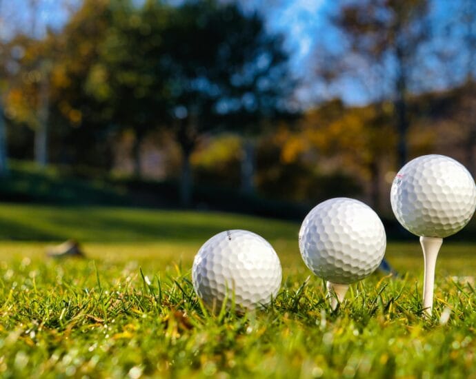 Three golf balls on tees ready for play on a bright sunny day in a green field.