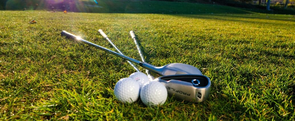 Photo of golf balls and clubs on a grassy course under bright sunlight, perfect for sports themes.