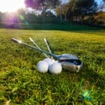 Photo of golf balls and clubs on a grassy course under bright sunlight, perfect for sports themes.