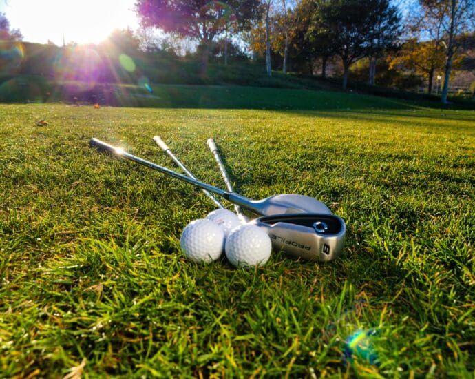 Photo of golf balls and clubs on a grassy course under bright sunlight, perfect for sports themes.