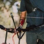 A person equipped with archery gear outdoors, holding a recurve bow ready to shoot.