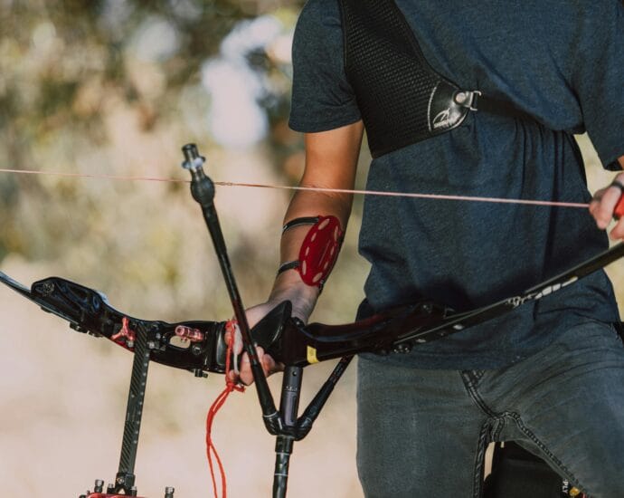 A person equipped with archery gear outdoors, holding a recurve bow ready to shoot.