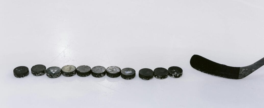 A row of hockey pucks and a stick on an ice rink, perfect for sports content.