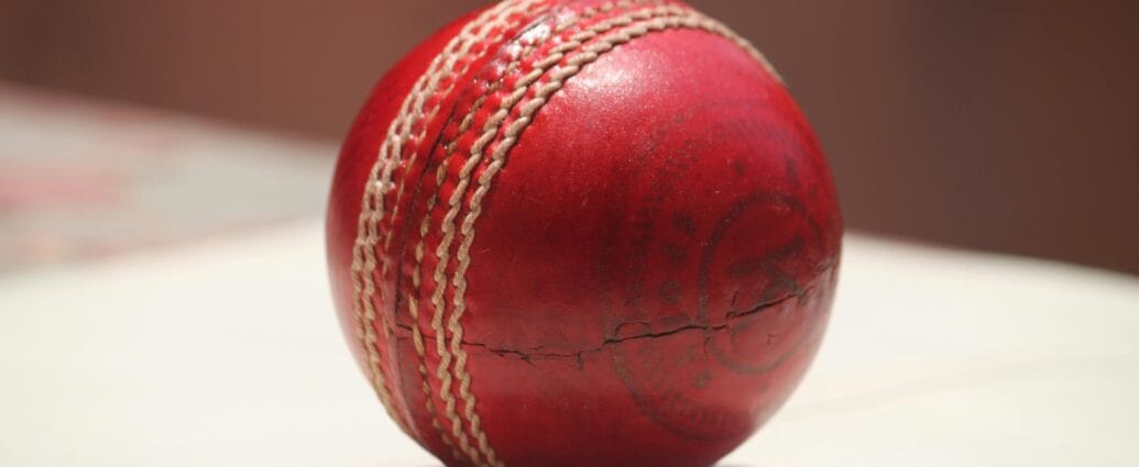 Detailed close-up of a red leather cricket ball showing wear and stitching.