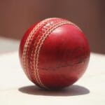 Detailed close-up of a red leather cricket ball showing wear and stitching.