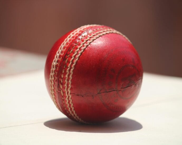 Detailed close-up of a red leather cricket ball showing wear and stitching.