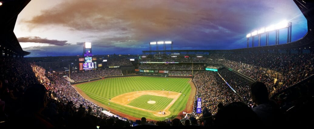 Wide-angle view of a baseball stadium at dusk capturing the field and excited crowd.