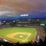 Wide-angle view of a baseball stadium at dusk capturing the field and excited crowd.