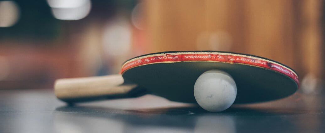 Close-up of a ping pong paddle and ball on a table with an artistic bokeh background, indoors.