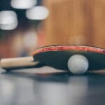 Close-up of a ping pong paddle and ball on a table with an artistic bokeh background, indoors.