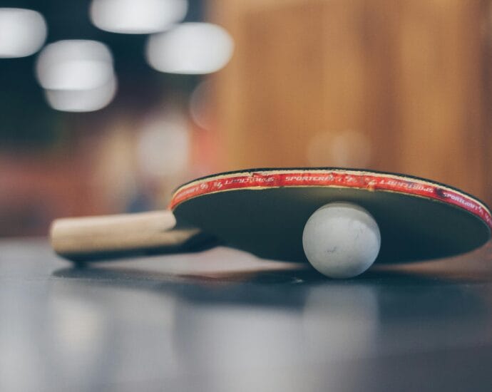 Close-up of a ping pong paddle and ball on a table with an artistic bokeh background, indoors.