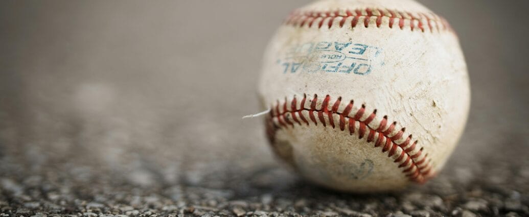 Detailed close-up of a worn baseball resting on a textured asphalt ground, emphasizing its use in sports.