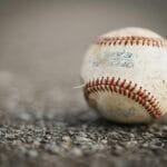 Detailed close-up of a worn baseball resting on a textured asphalt ground, emphasizing its use in sports.