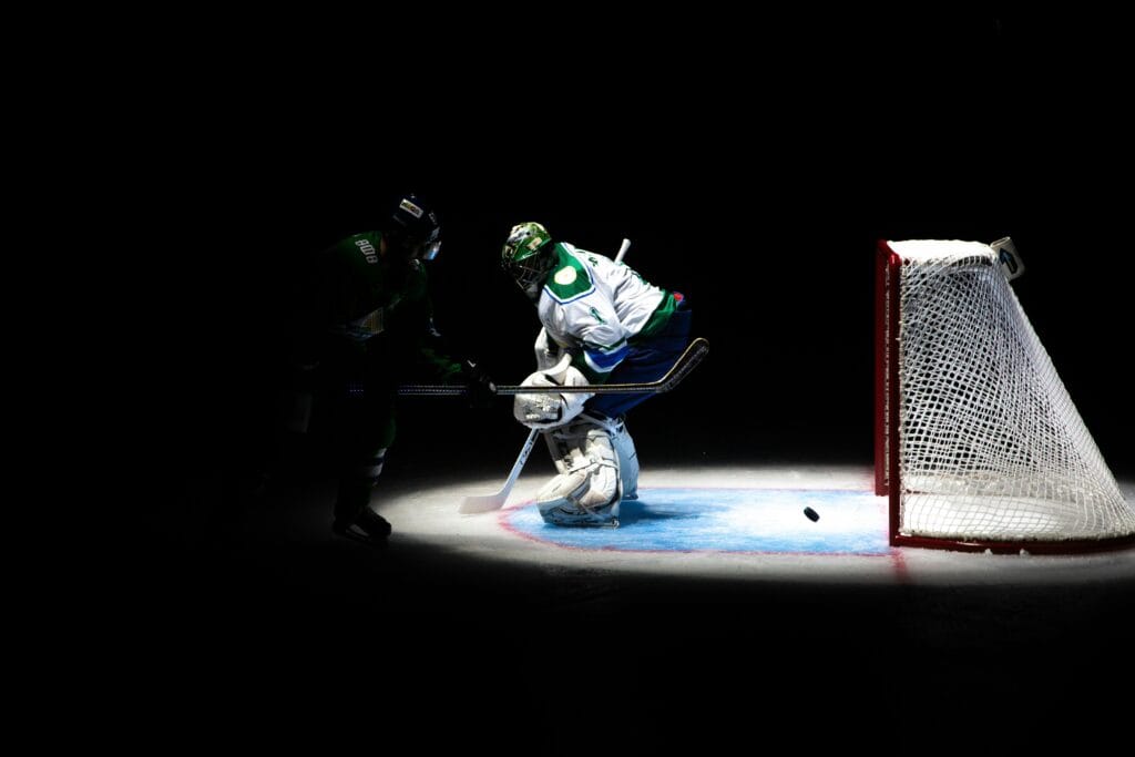 Intense ice hockey action with players competing near the goal in dramatic lighting.