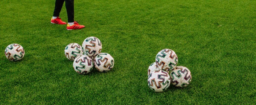 Pile of soccer balls on a green field with a person preparing for training session.