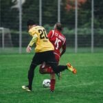 Two soccer players in action on a vibrant green field during a daytime match.